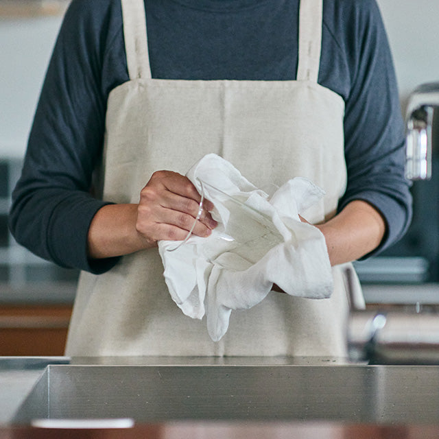 Person wearing a beige apron holding a white cloth in a kitchen setting