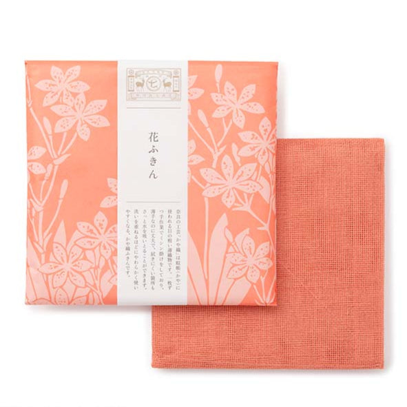 Coral coloured tea towel packed in floral design wrapping paper on a white background