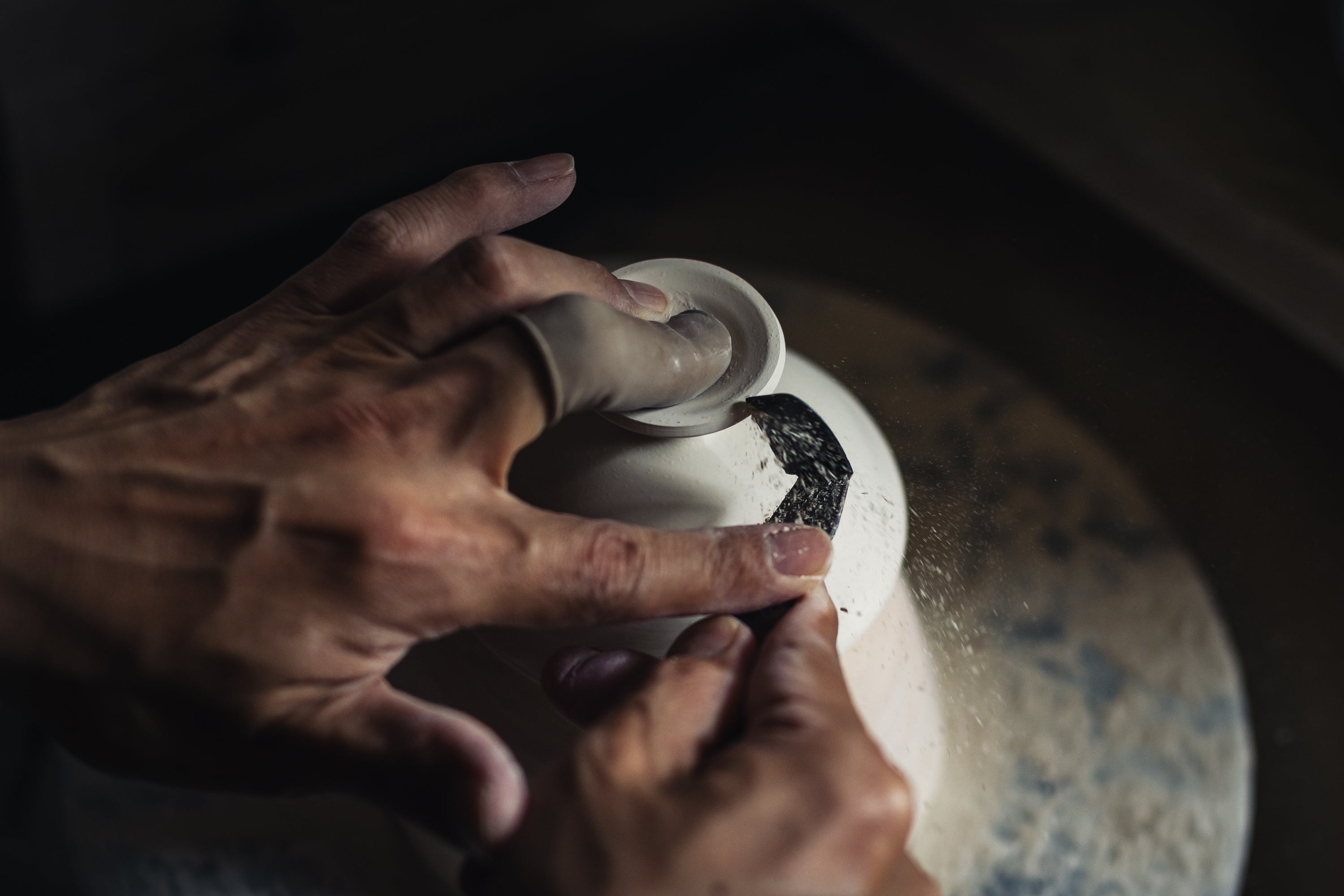 Person's hands working on a ceramic piece with a dark background