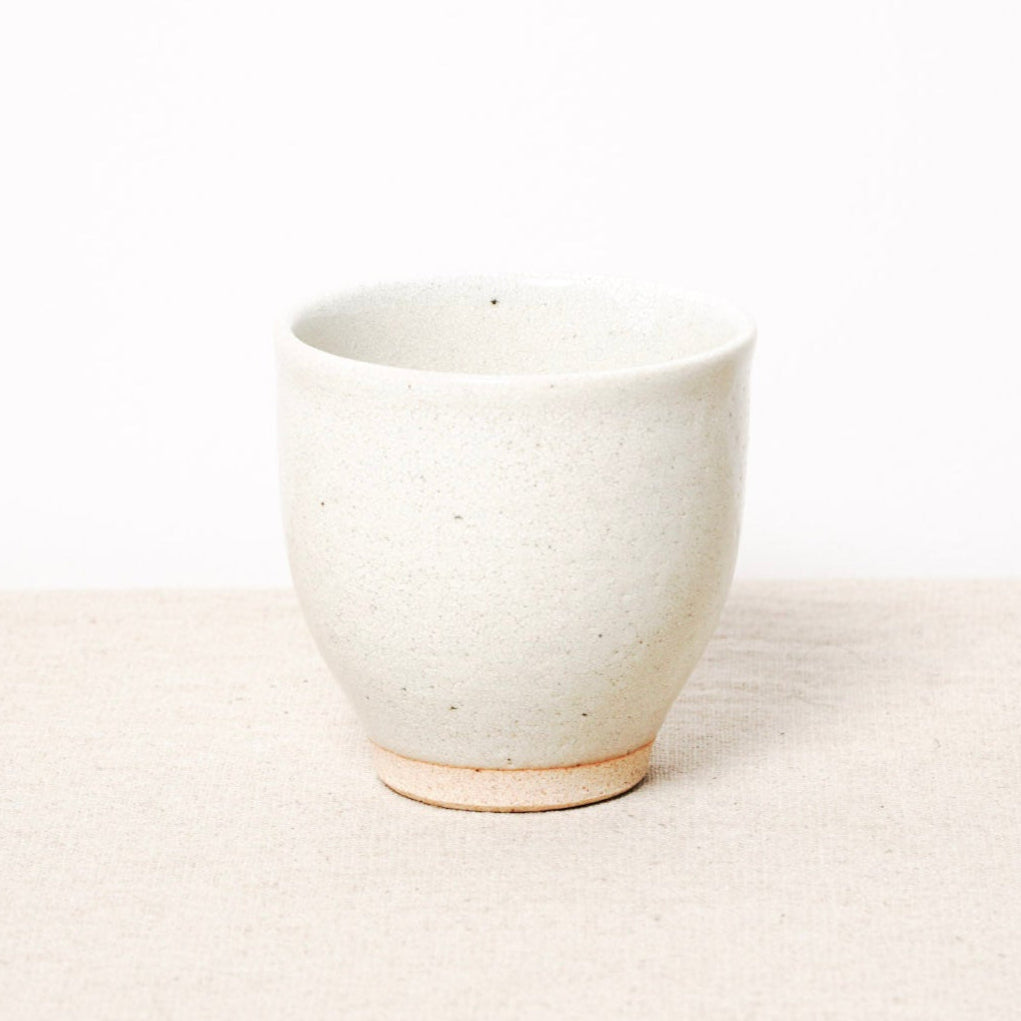 White ceramic cup on a light beige surface with a white background