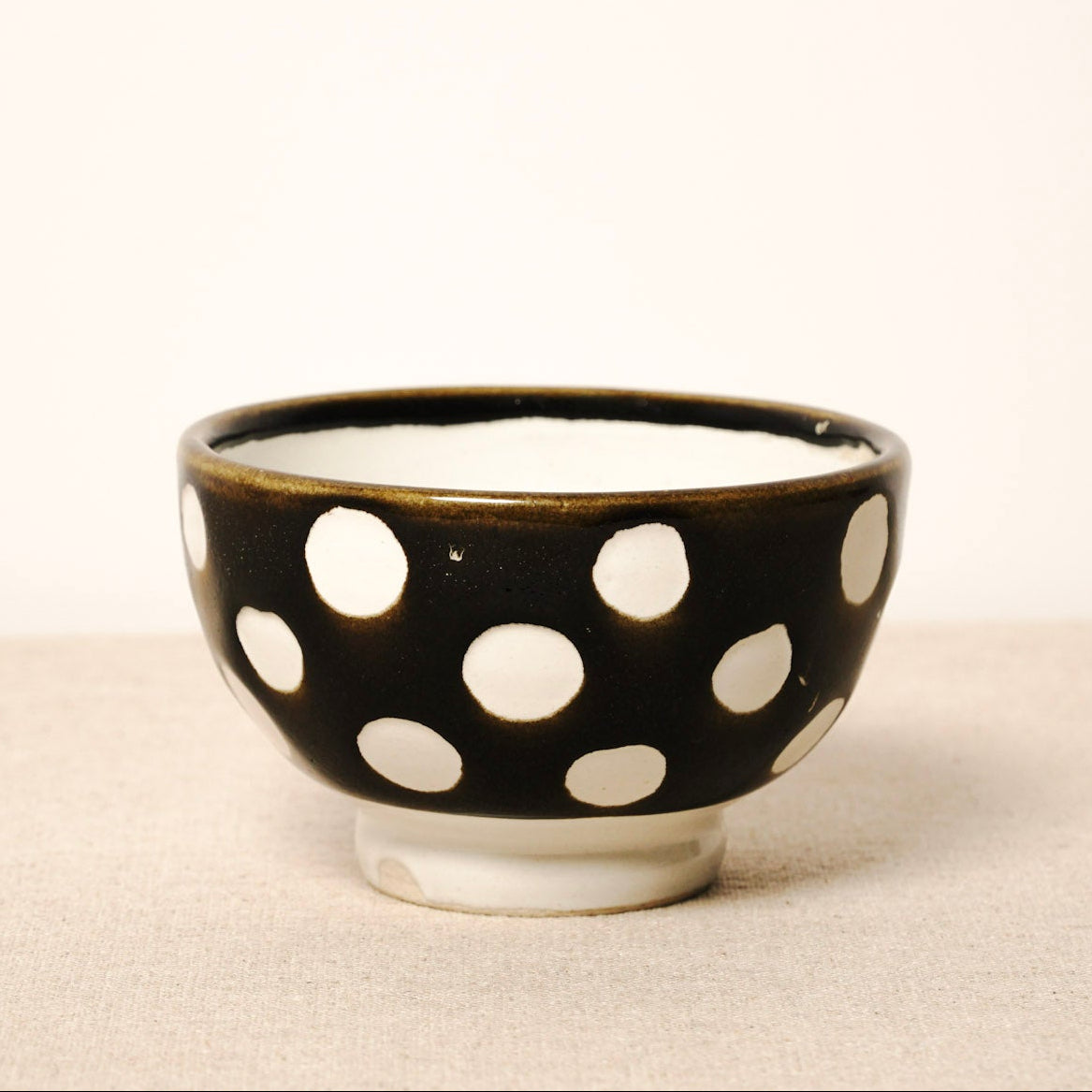 Black ceramic bowl with white polka dots on a beige surface