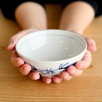 Person holding a small white bowl with blue floral patterns on a wooden surface