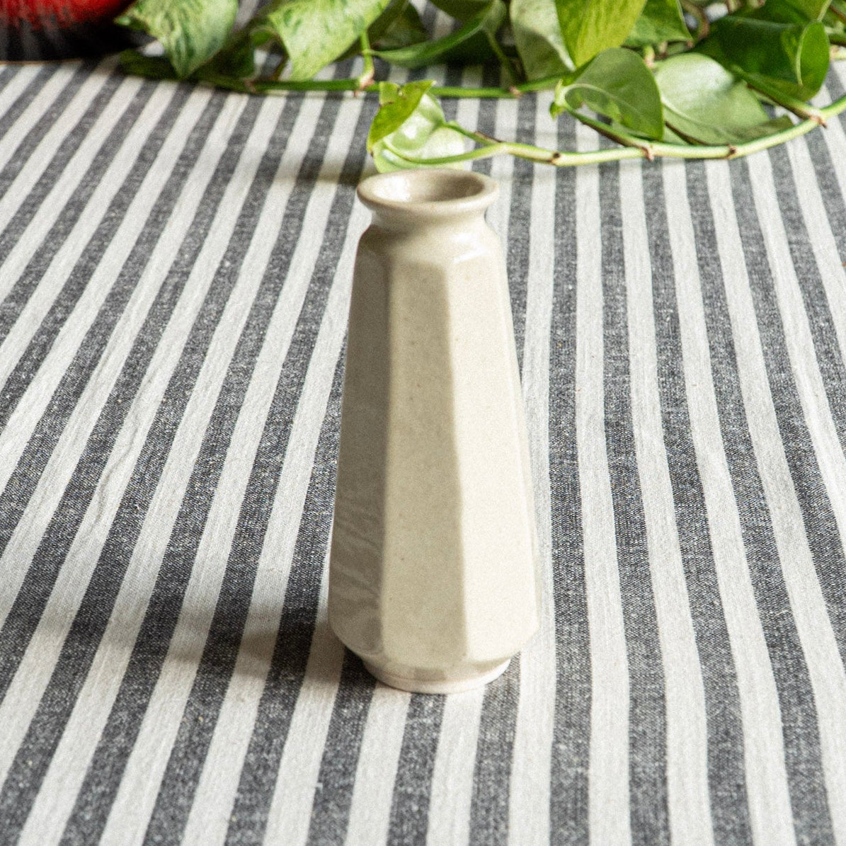 White ceramic vase on a striped tablecloth with green leaves in the background