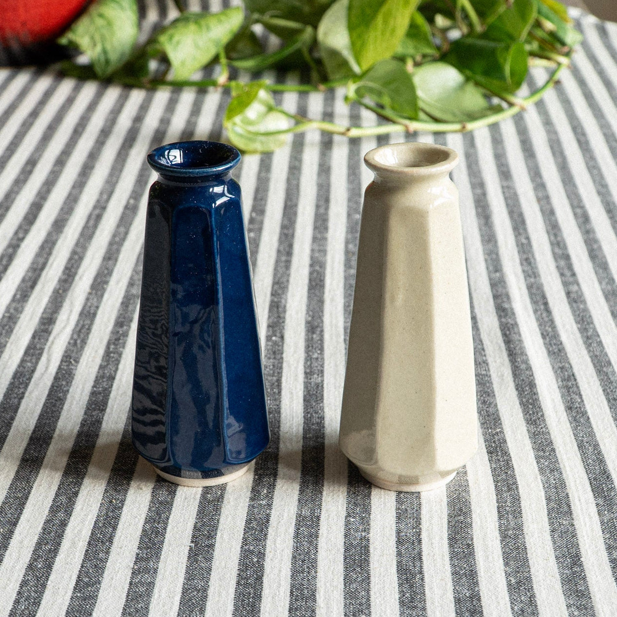 Two ceramic vases, one blue and one beige, on a striped tablecloth.