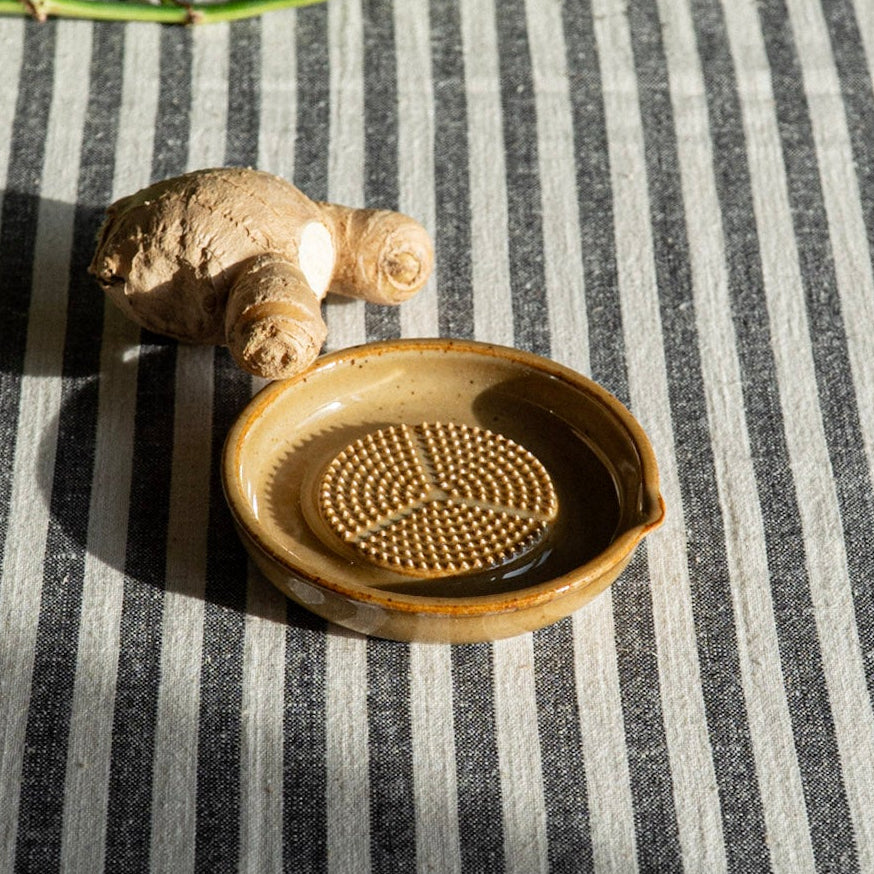 Ceramic grater  and ginger on a striped fabric surface