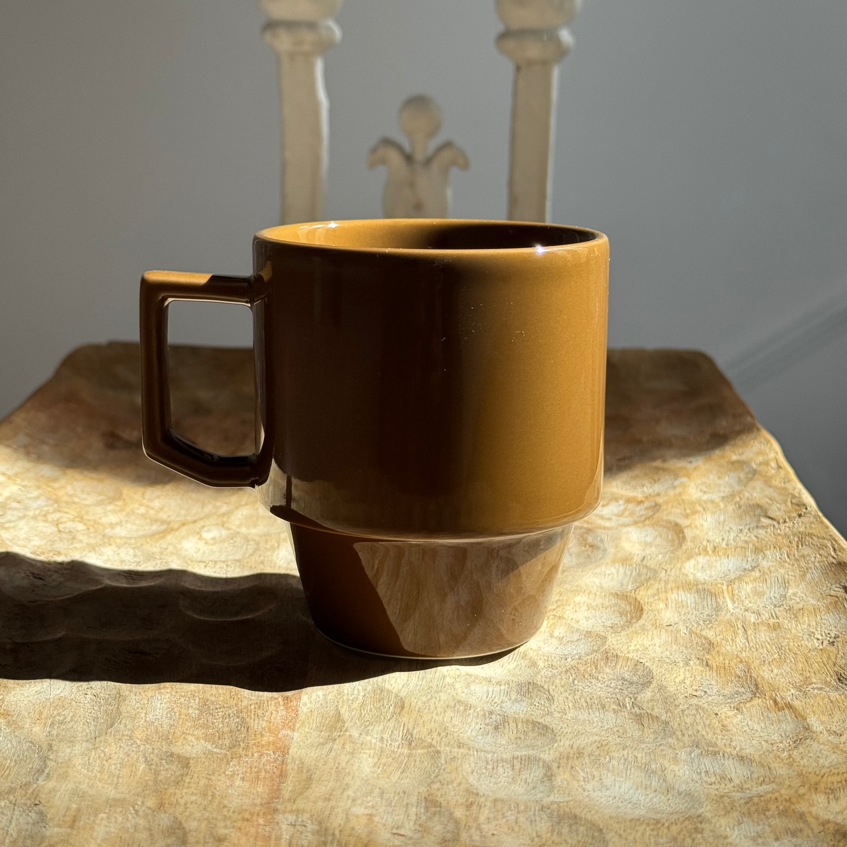 Brown ceramic mug on a textured surface with a decorative chair in the background