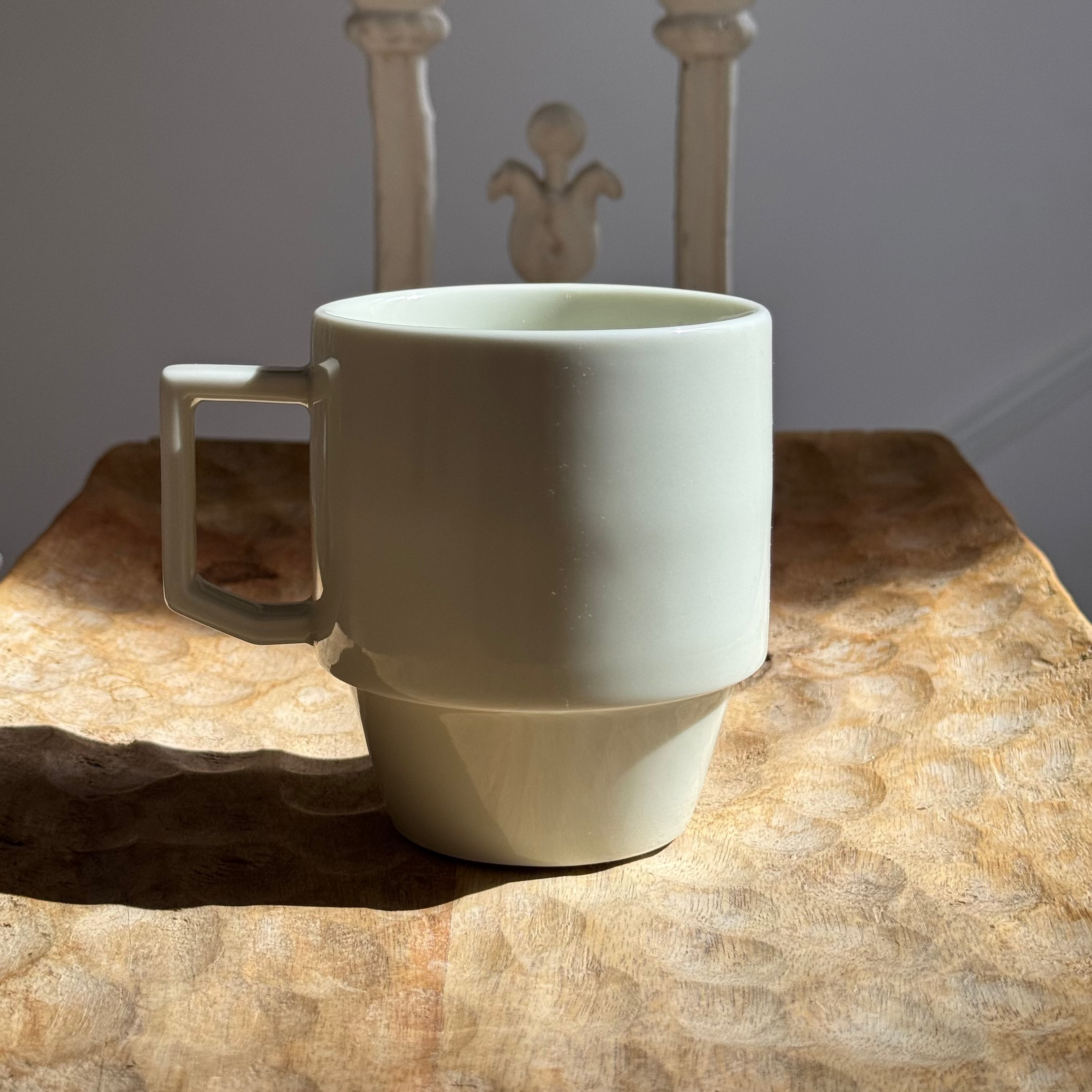 cream white ceramic mug on a wooden surface with a decorative chair in the background