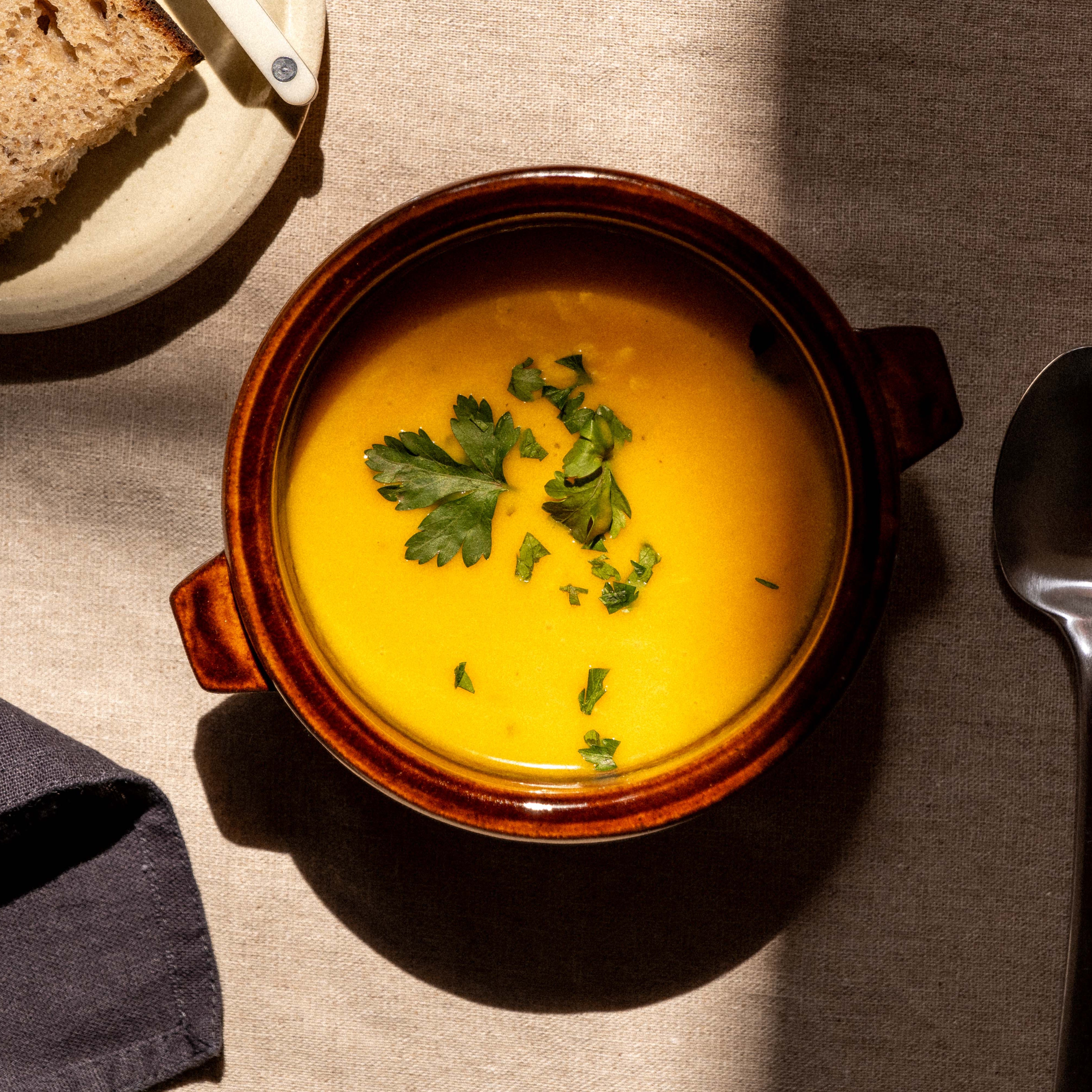 Bowl of soup with bread and a spoon on a table