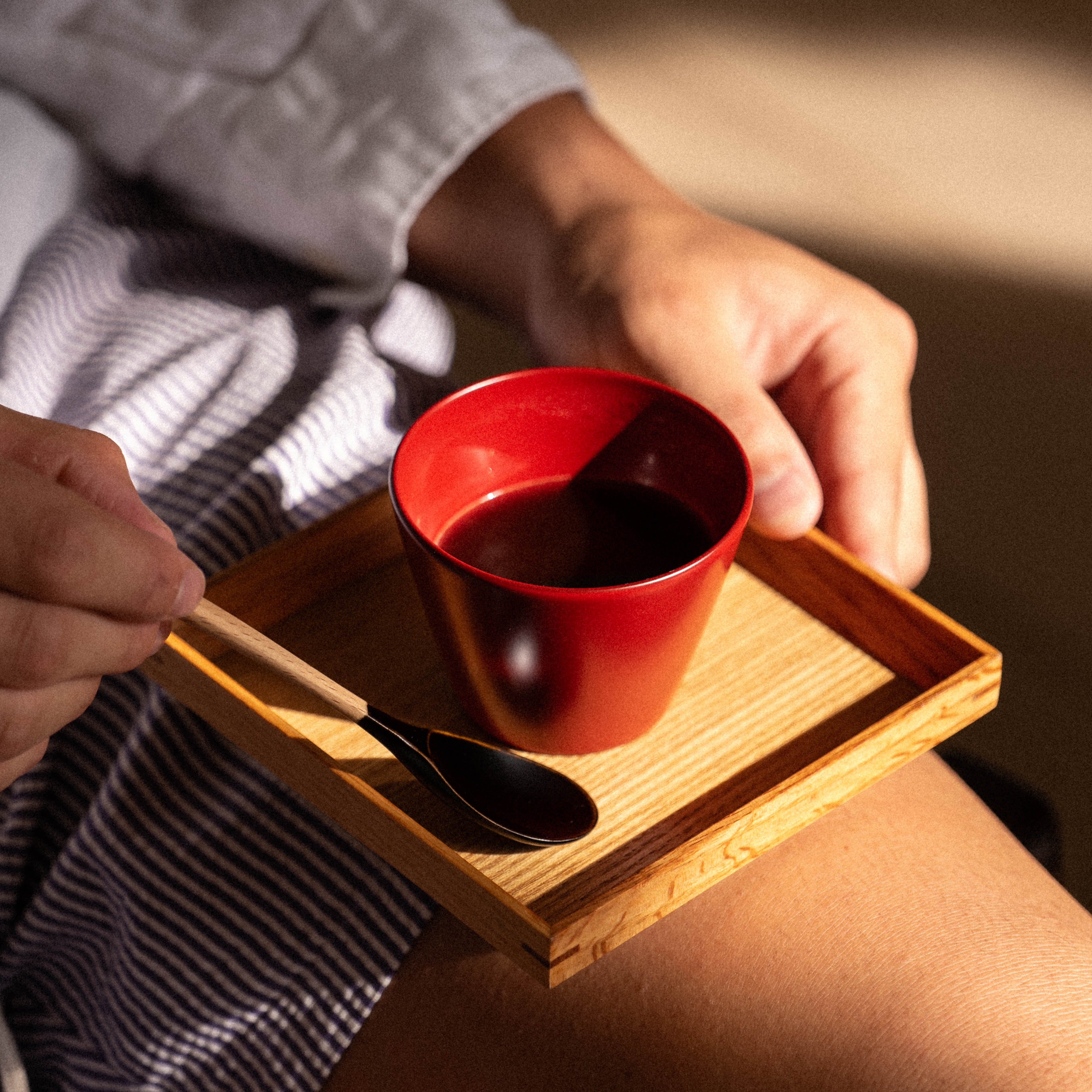 Person holding a red cup with a wooden tray on their lap