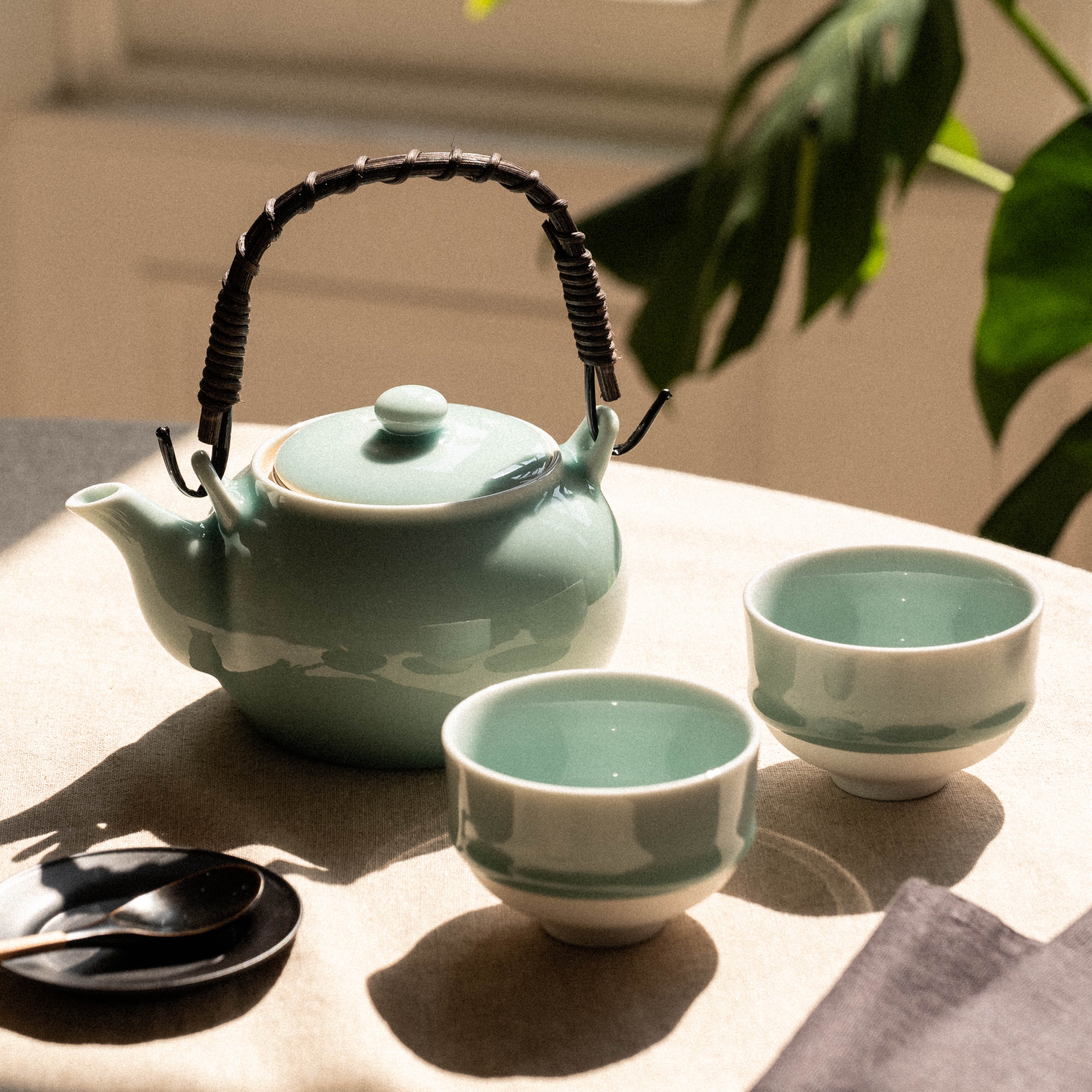 Tea set with a teapot and two cups on a table with a plant in the background