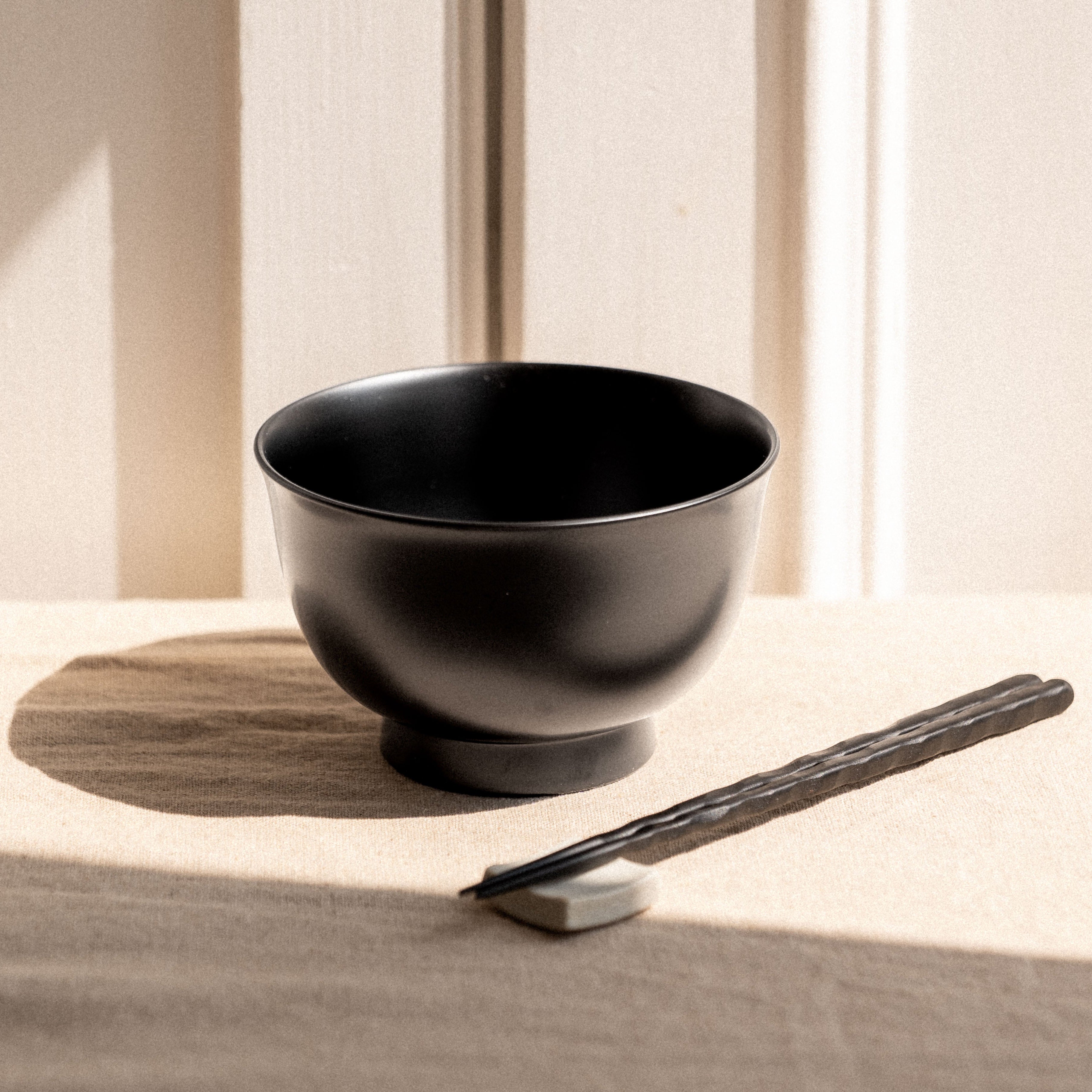 Black ceramic bowl and chopsticks on a wooden surface with a neutral background