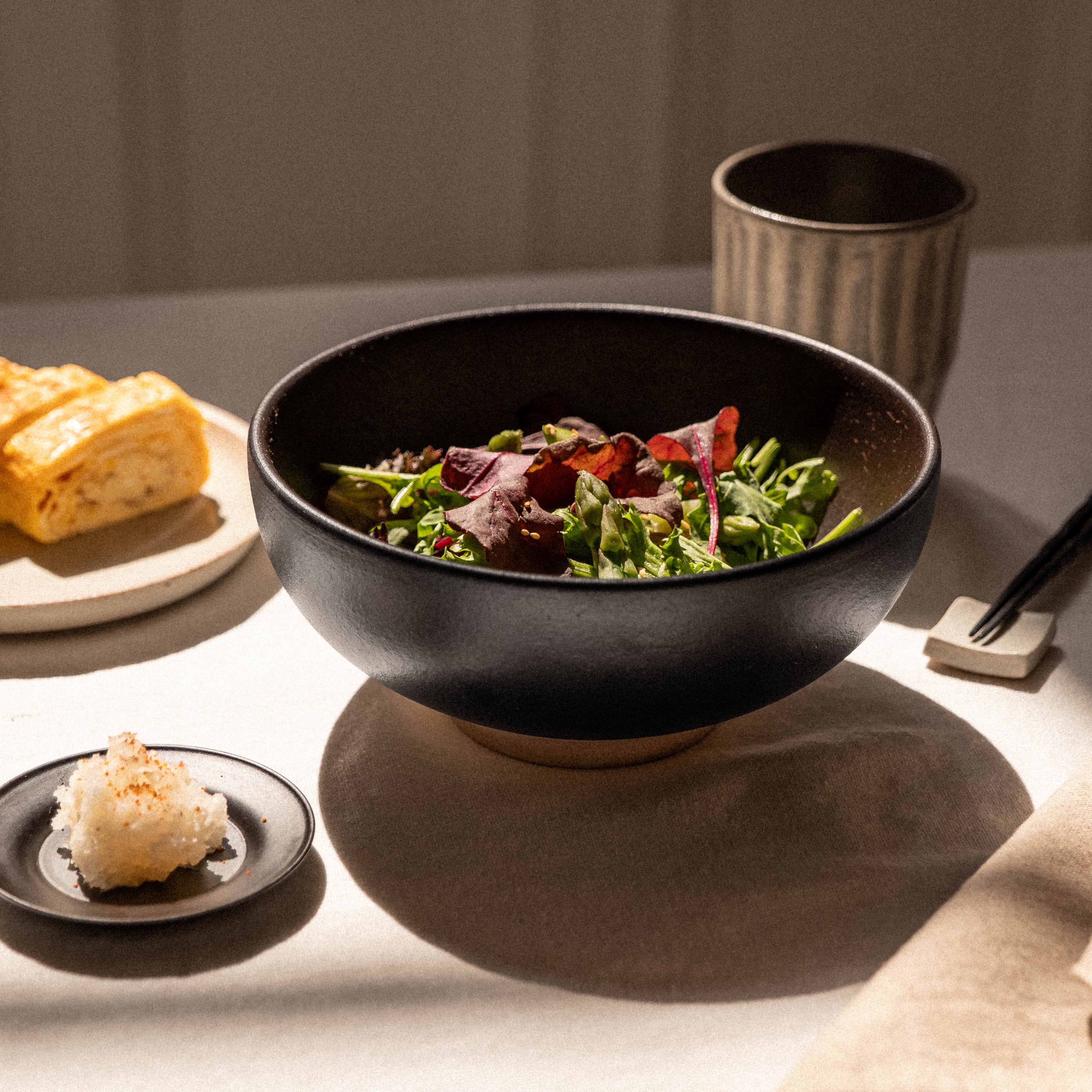 Bowl of salad with a side of bread and a small dish on a table.