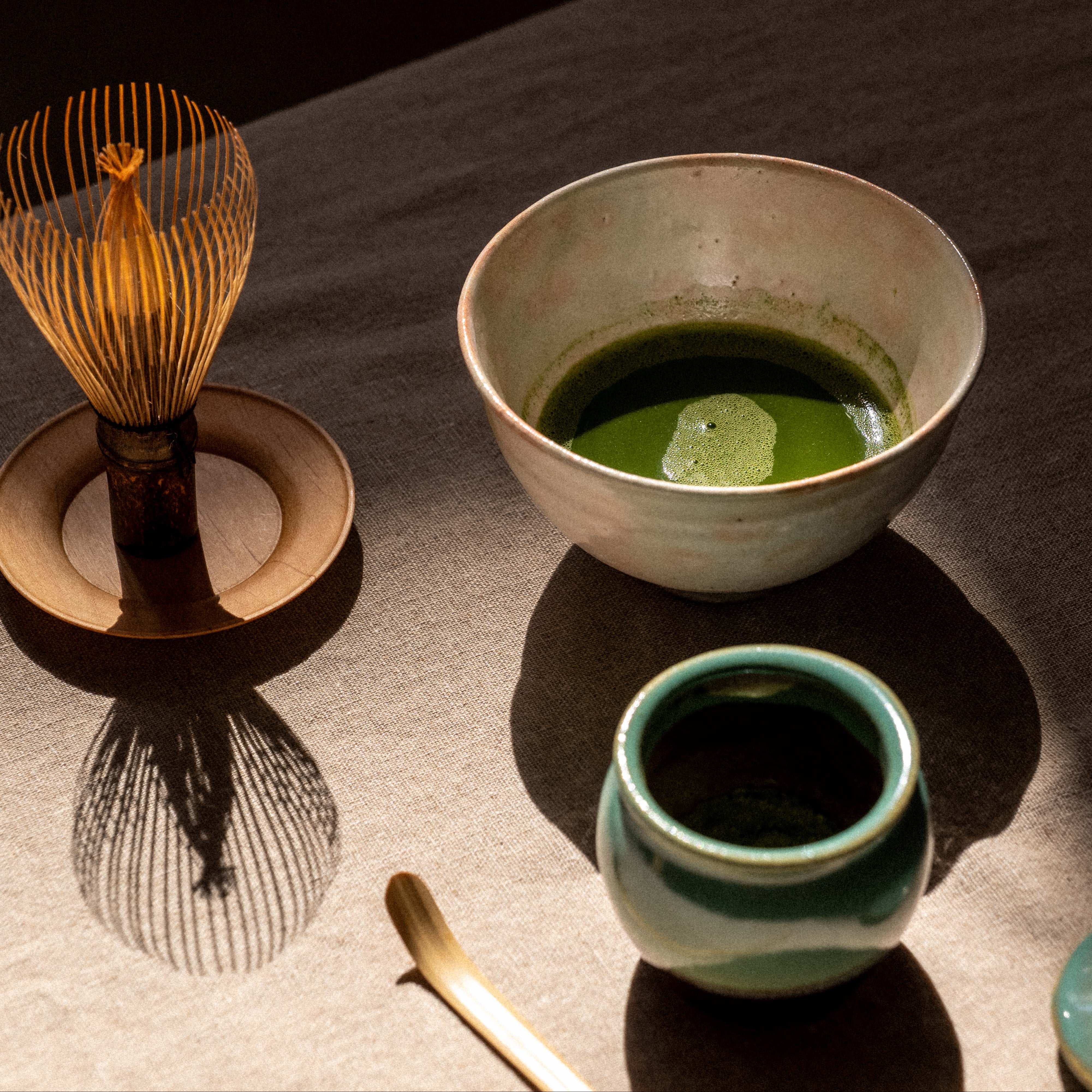 Ceramic bowl with green tea and accessories on a reflective surface