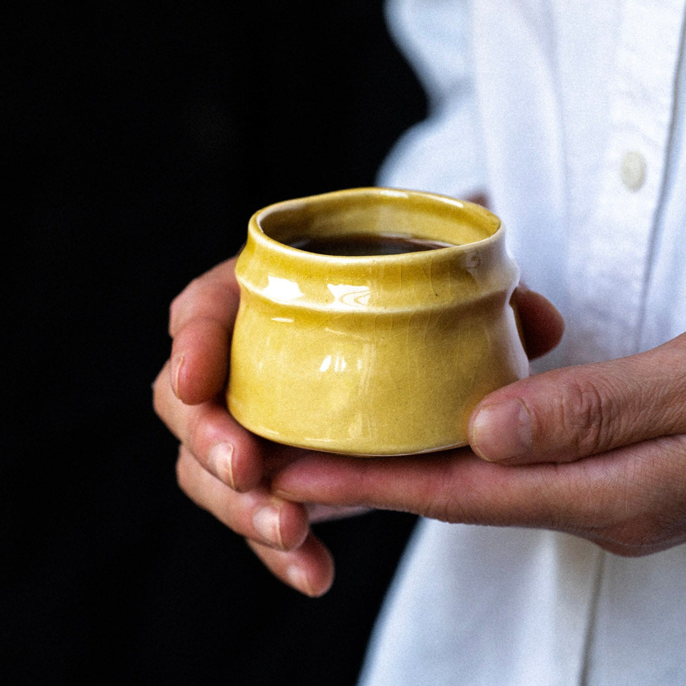 Hand holding a yellow ceramic container against a dark background