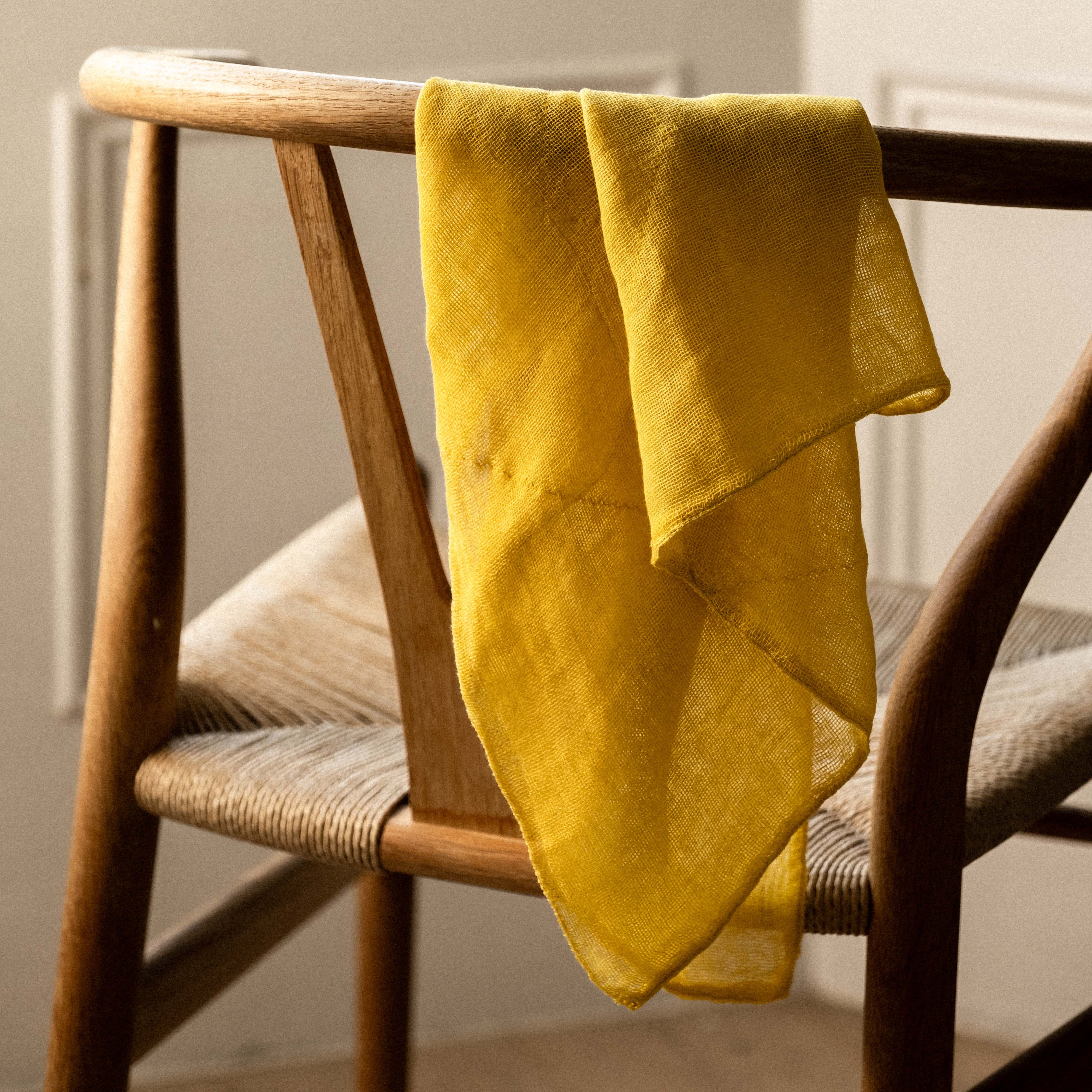 Yellow tea towel draped over a wooden chair with a neutral background