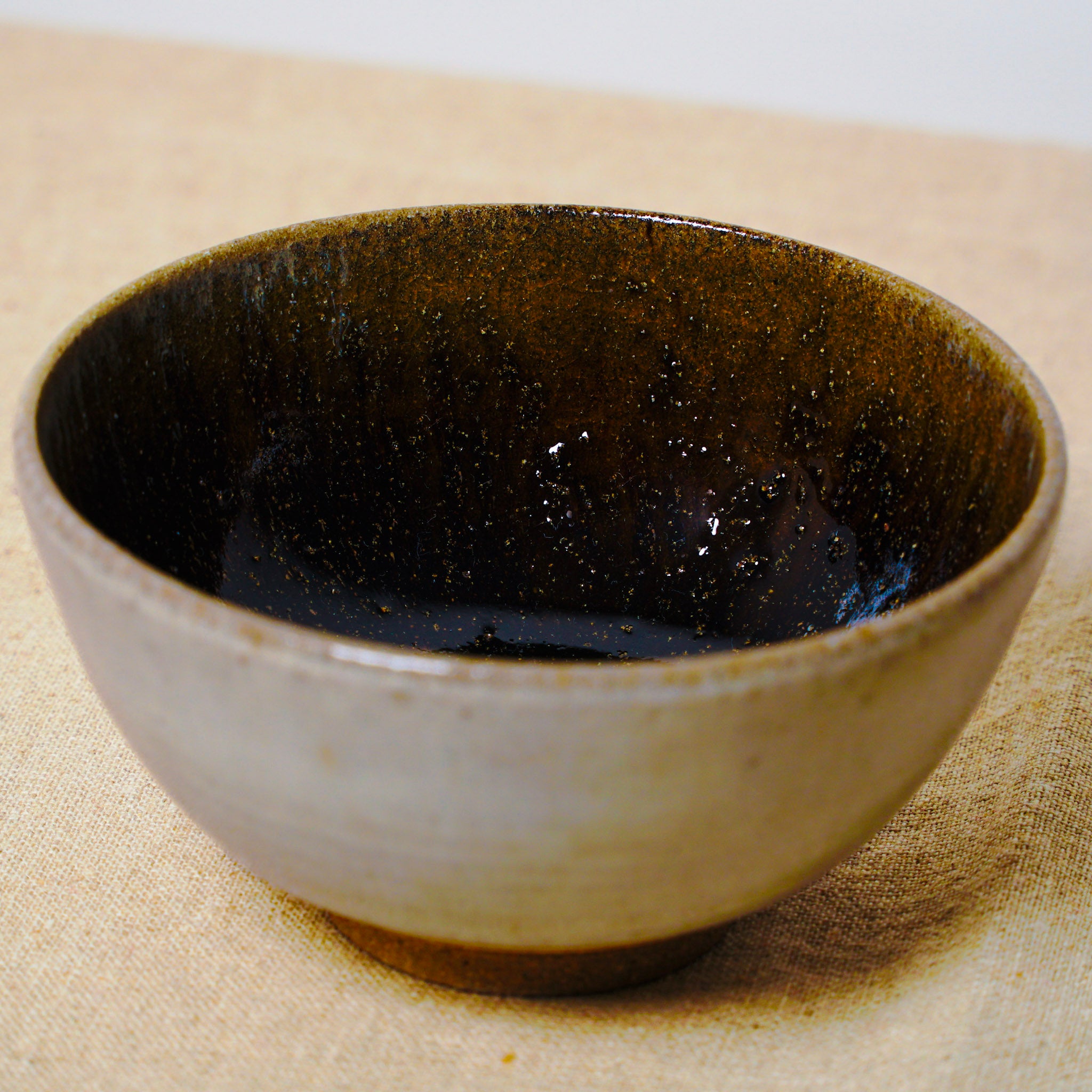 Ceramic bowl with black interior and beige exterior on a textured surface