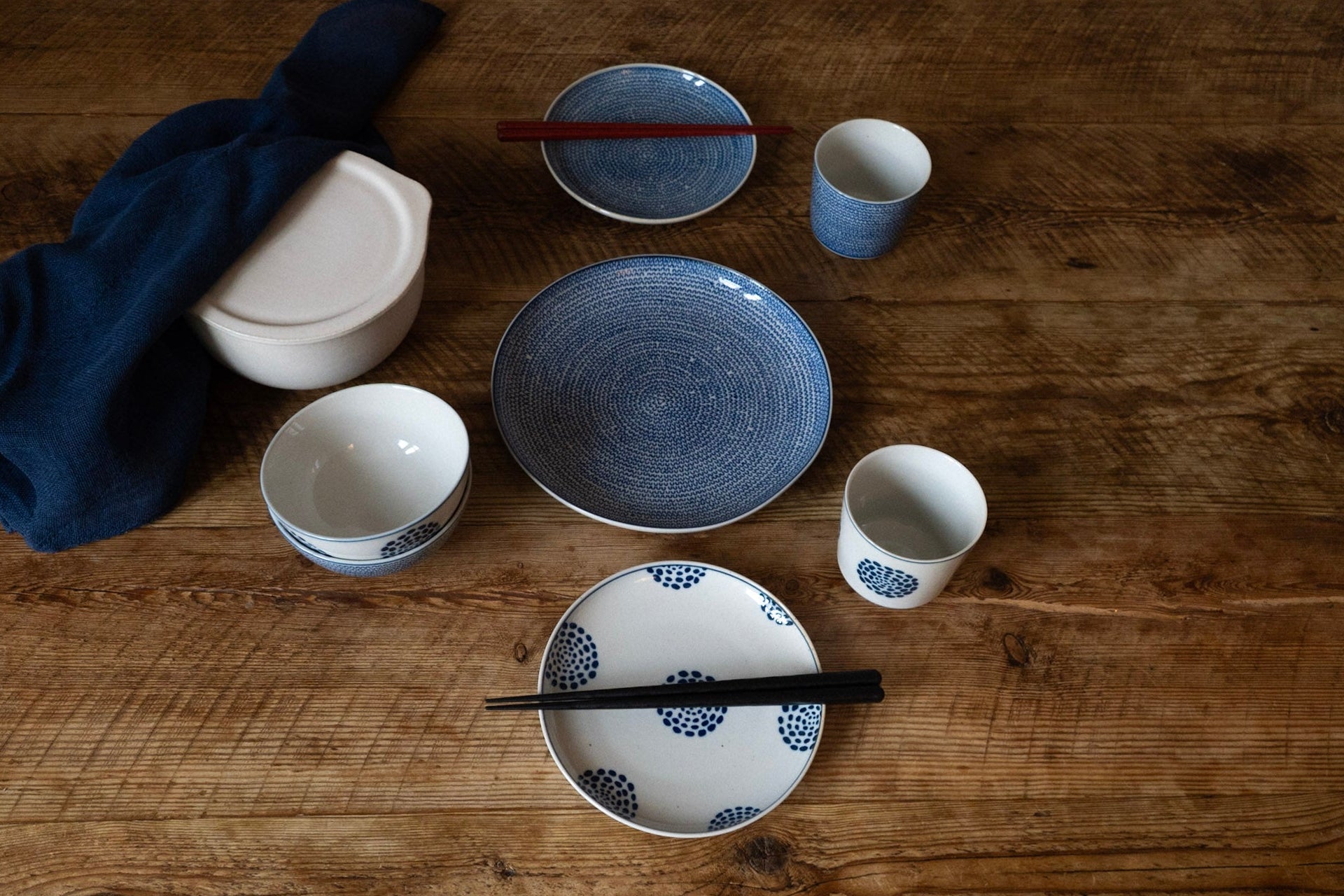 Set of ceramic dishes and cups on a wooden table with chopsticks.