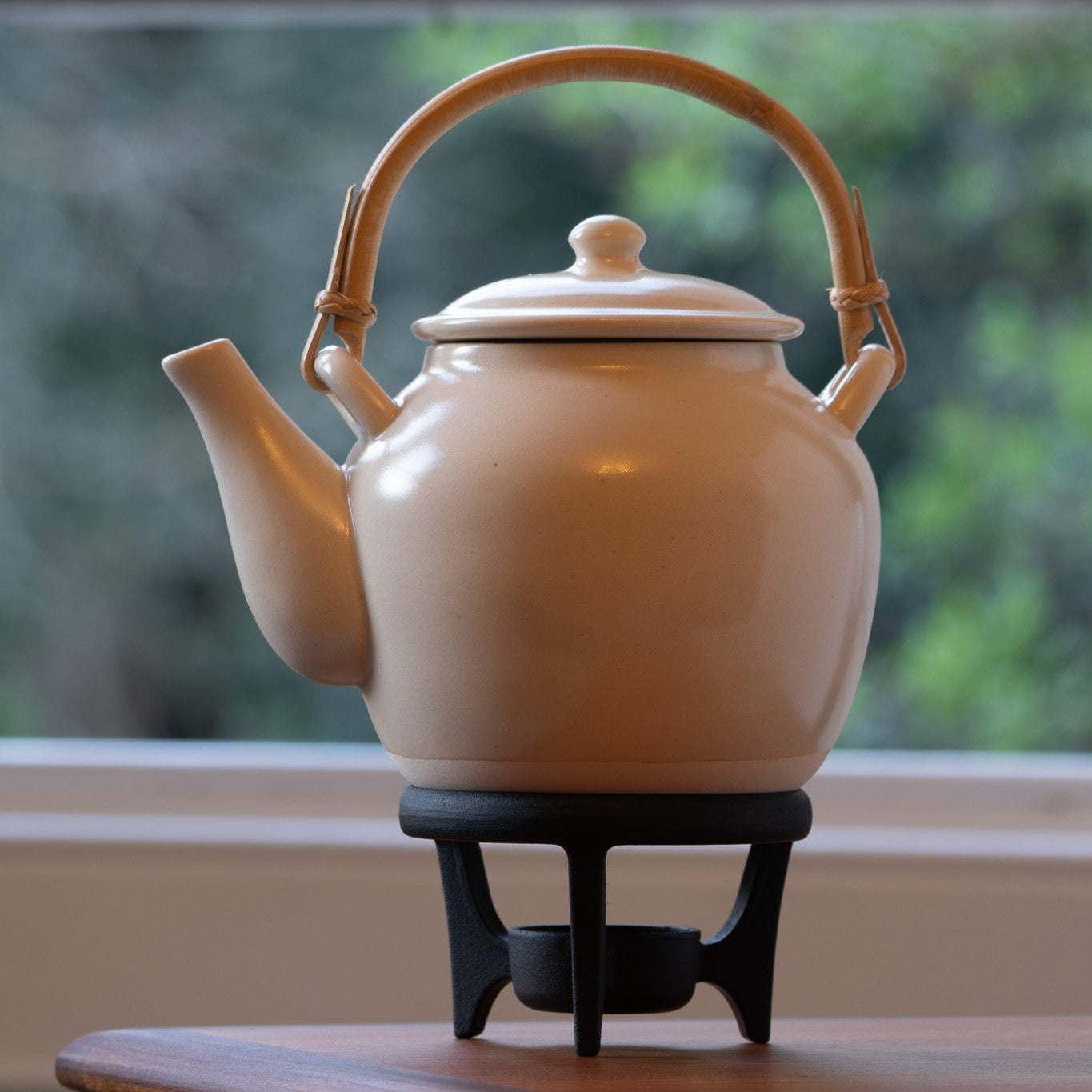Beige teapot on a black stand with a blurred green outdoor background