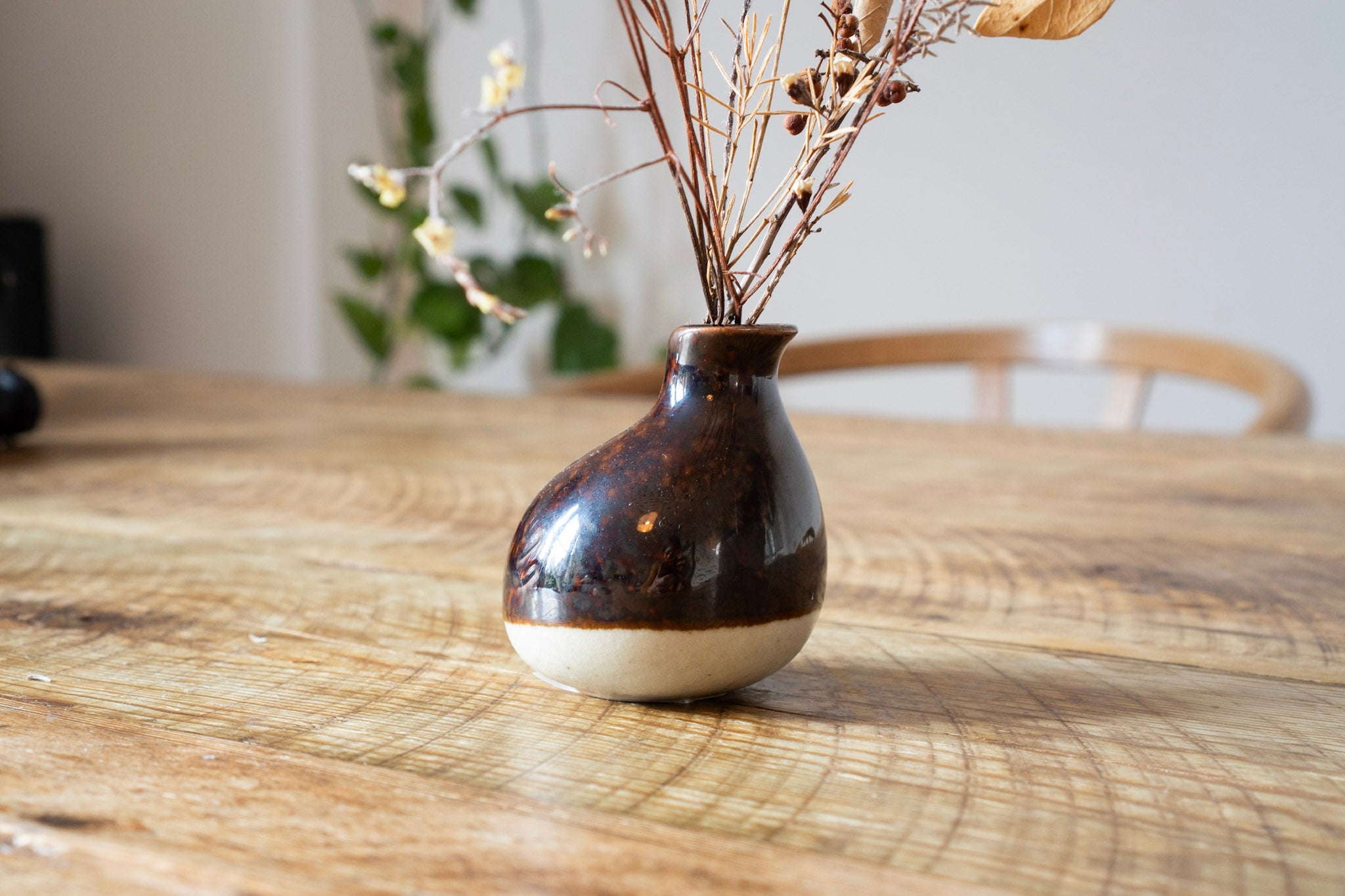 Small brown and white ceramic vase with dried plants on a wooden table