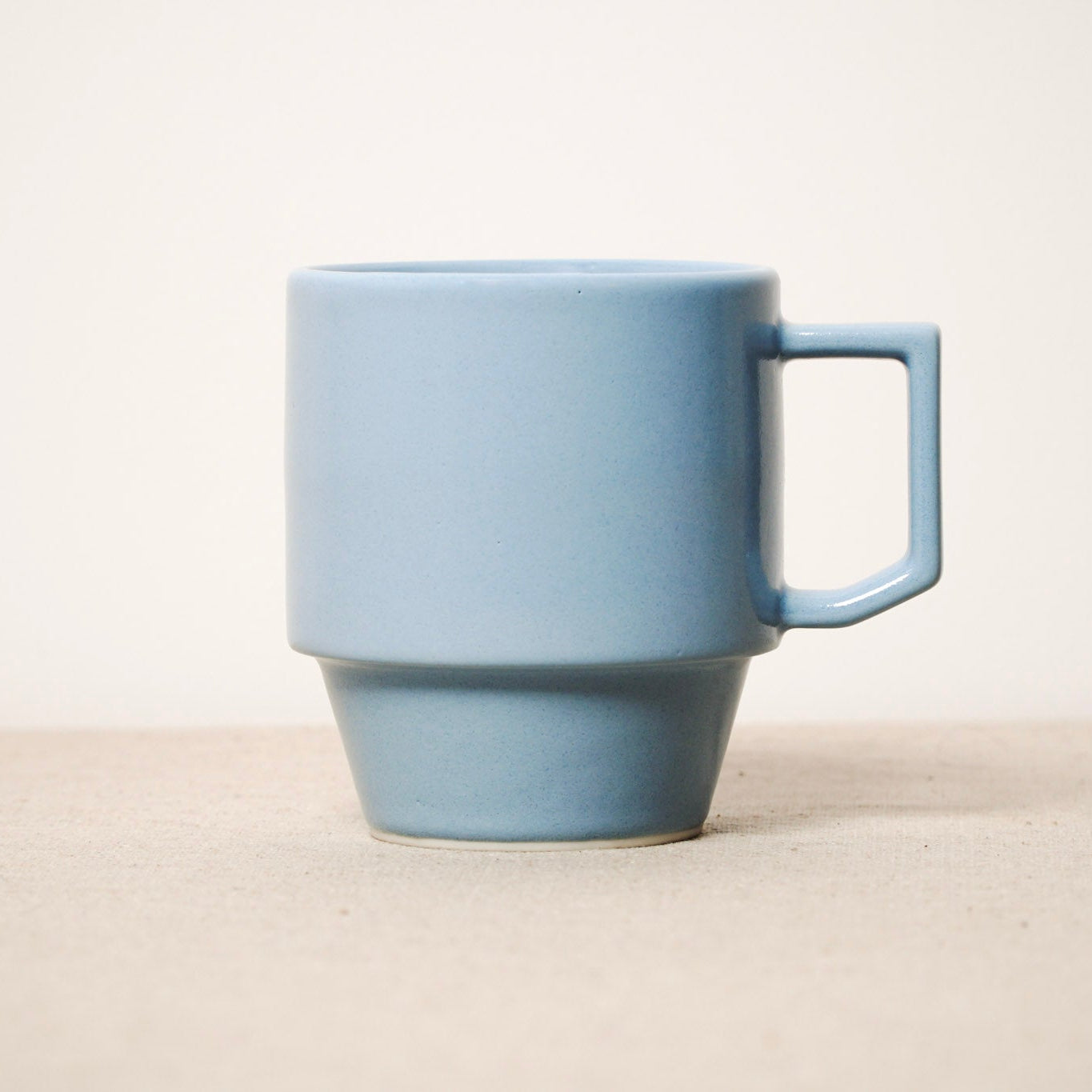 Light blue ceramic mug on a beige surface with a white background
