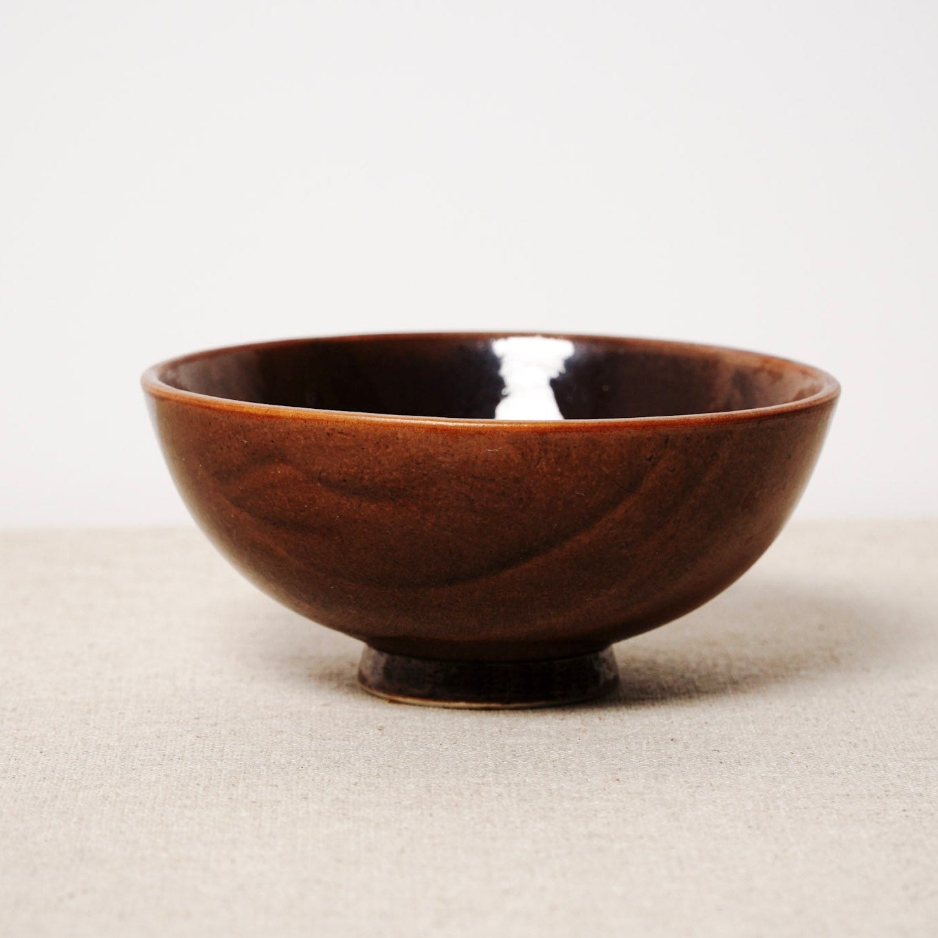 Brown ceramic bowl on a beige surface with a white background