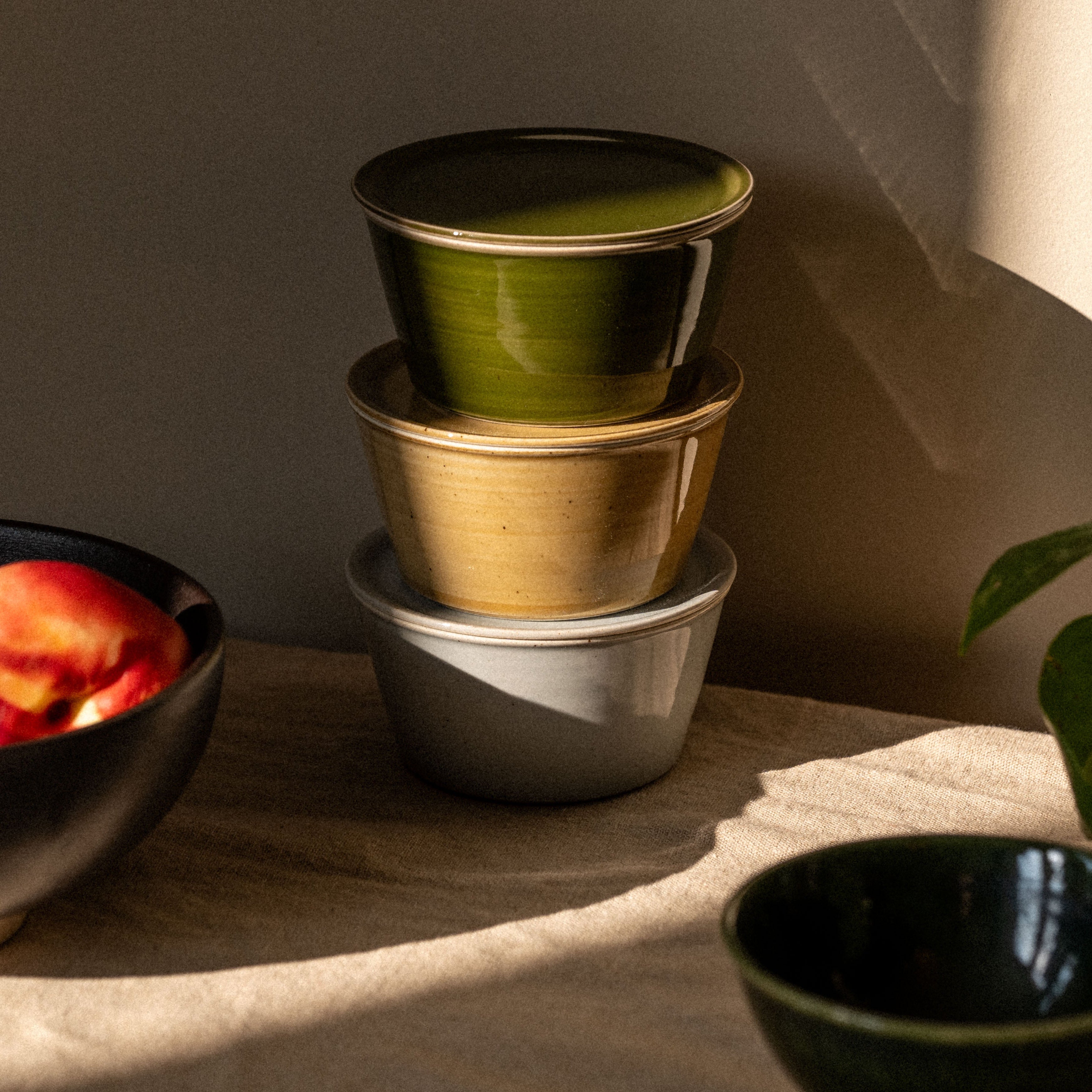 Stack of colorful ceramic bowls on a wooden surface with a plant in the background
