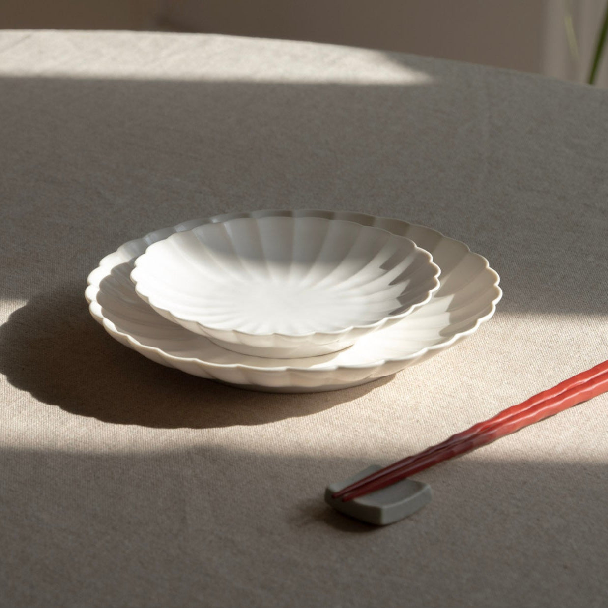 Two white ceramic plates stacked on a light gray surface with red chopsticks beside them.