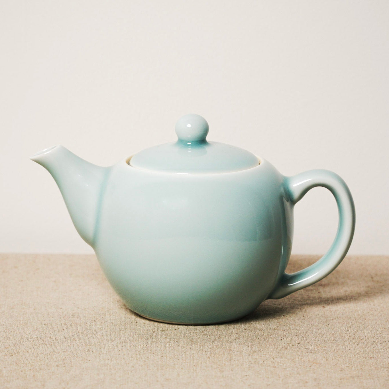 Light blue ceramic teapot on a beige surface with a white background