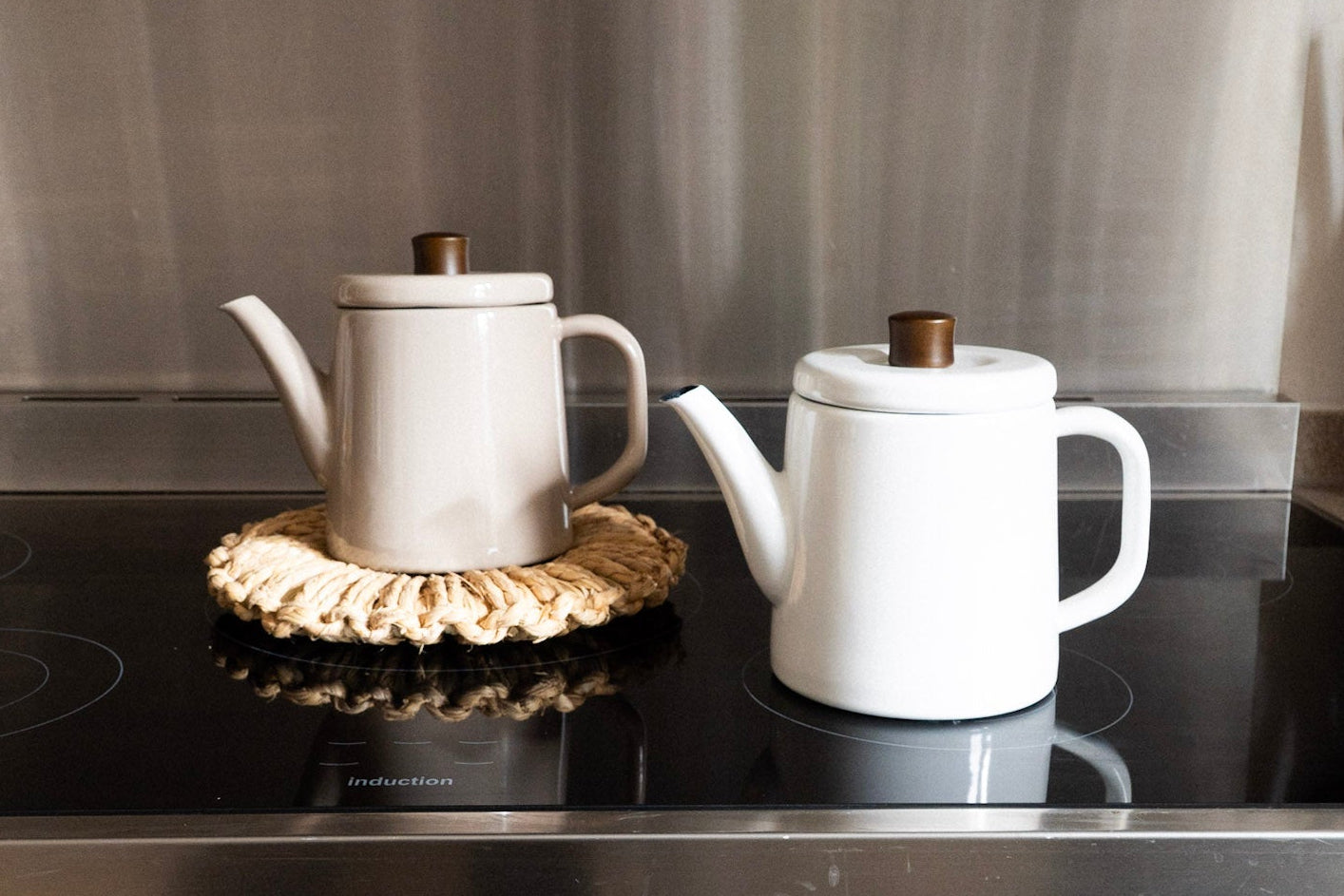 Two white teapots on a stovetop with a digital clock displaying the time.