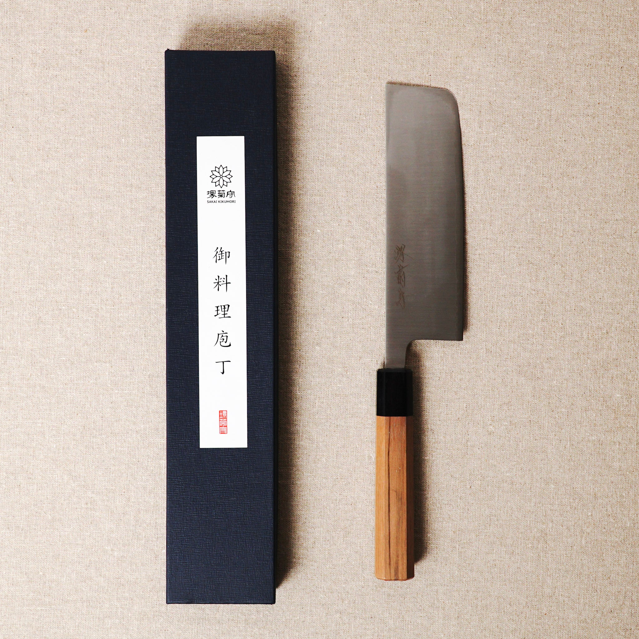 Japanese knife with wooden handle next to its packaging on a beige surface
