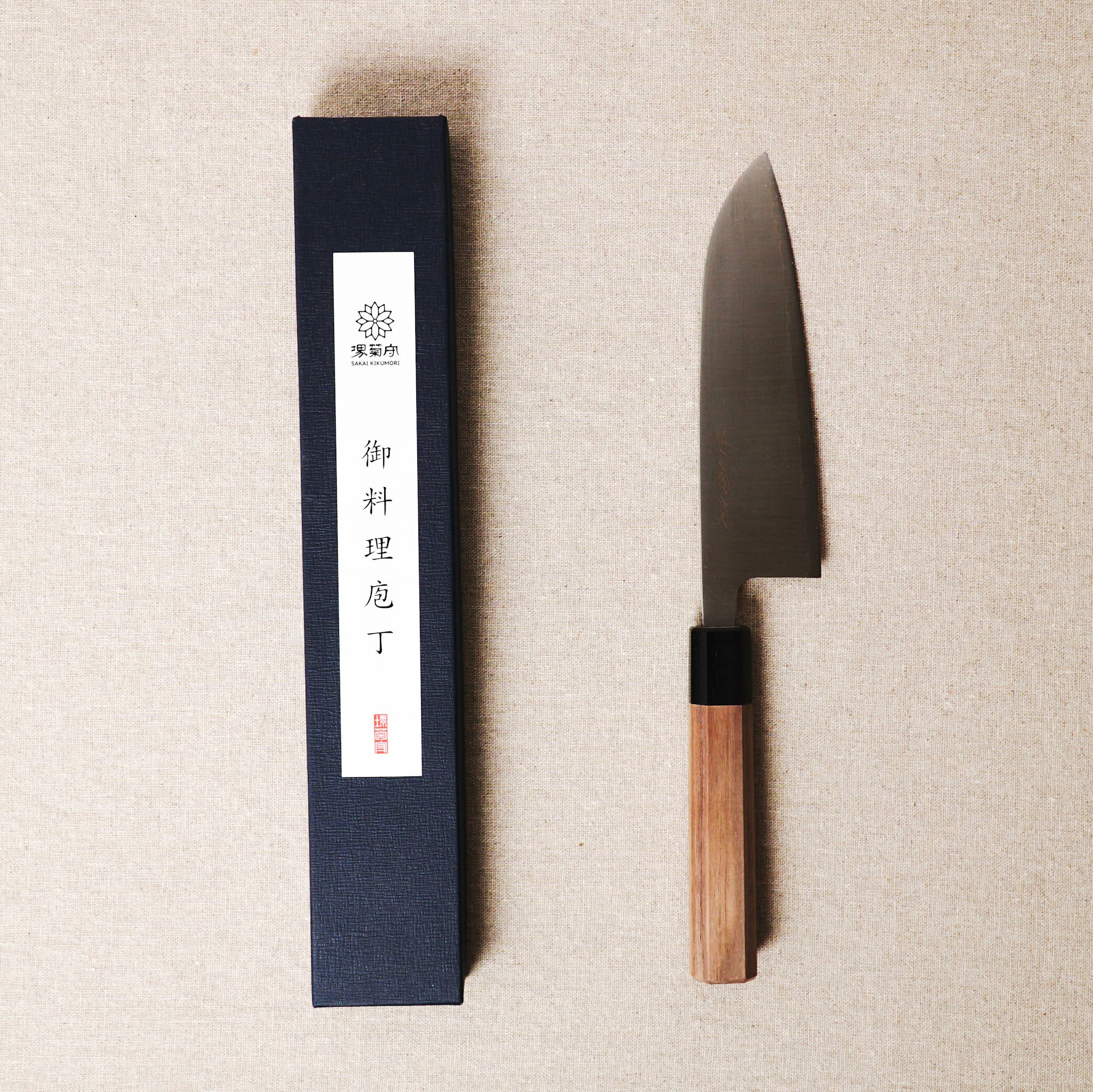 Sleek knife with wooden handle and black sheath on beige fabric background