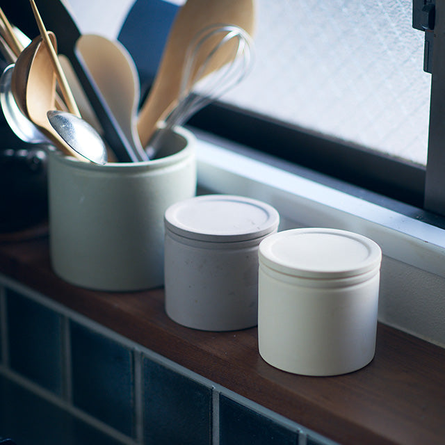 Two white ceramic jars with lids on a wooden surface near a window.
