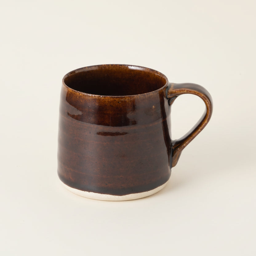 Brown ceramic mug on a light surface with a blurred green outdoor background