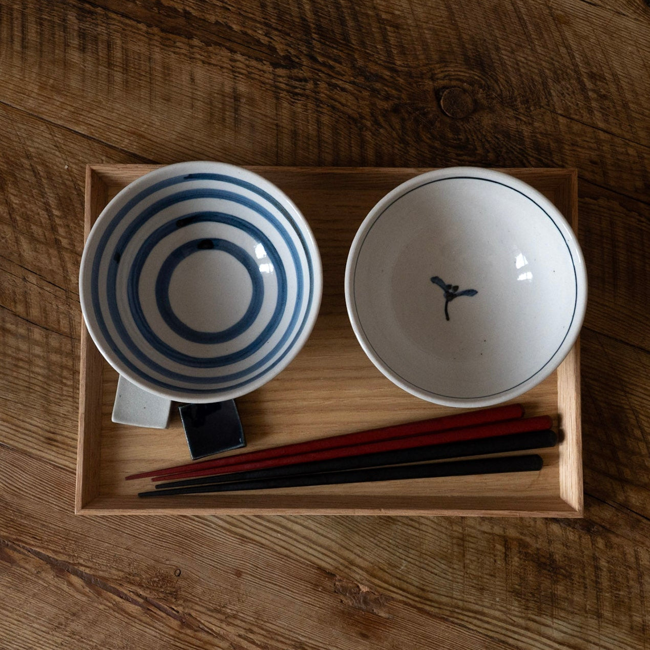 Two ceramic bowls with chopsticks in a wooden box on a wooden surface